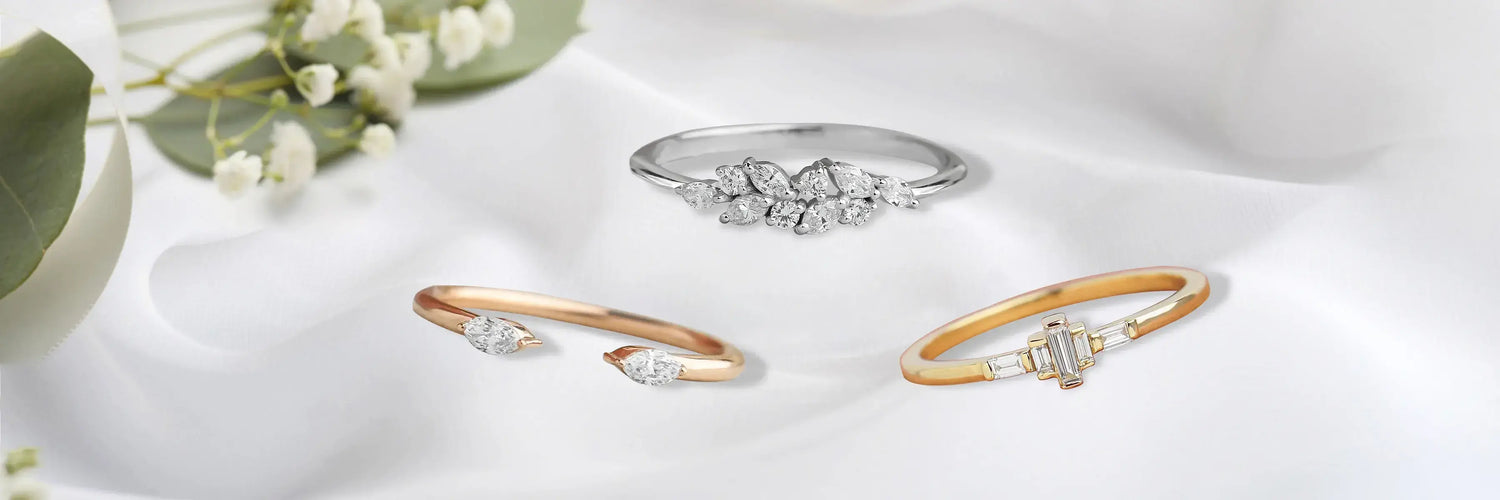 Dainty lab-grown diamond engagement rings in yellow gold — graduated baguette cluster ring, emerald cut three-stone with round brilliant side stones, and linear baguette bar solitaire on layered beige stone steps