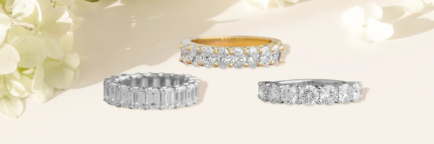 Three lab-grown diamond eternity bands in yellow gold — pear cut shared prong full eternity band, curved baguette chevron wedding band, and alternating baguette and round brilliant half eternity band on olive green background