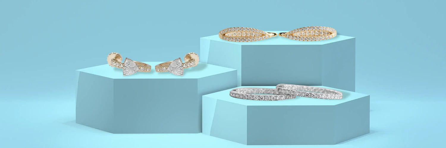 Pairs of lab-grown diamond earrings on navy displays — yellow gold pavé dome hoop earrings, white gold open fan-shaped ear climbers, and yellow gold marquise sunburst open hoop earrings on dark blue background