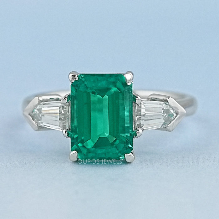 front view of emerald gemstone and bullet-cut diamond three-stone engagement ring