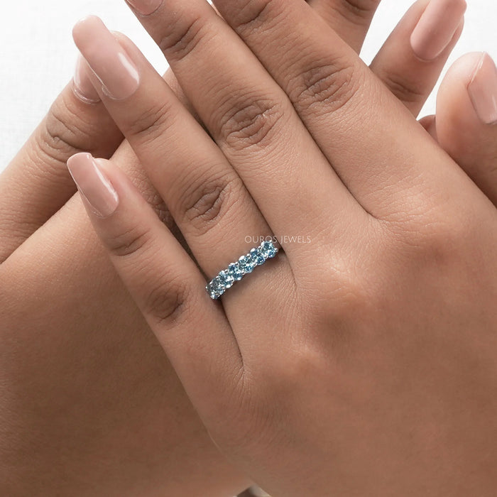 blue oval-cut seven stone lab diamond wedding band on model's finger