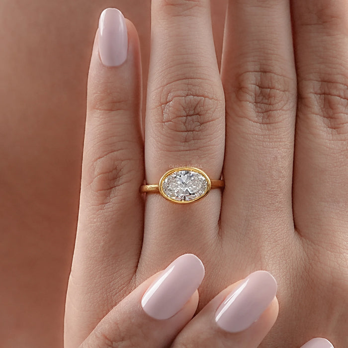 east west oval cut bezel set diamond solitaire ring in women's hand