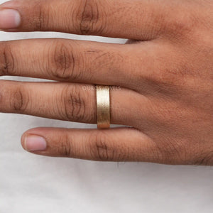 A Men wearing Brushed Gold Ring in ring finger shows on white surface.