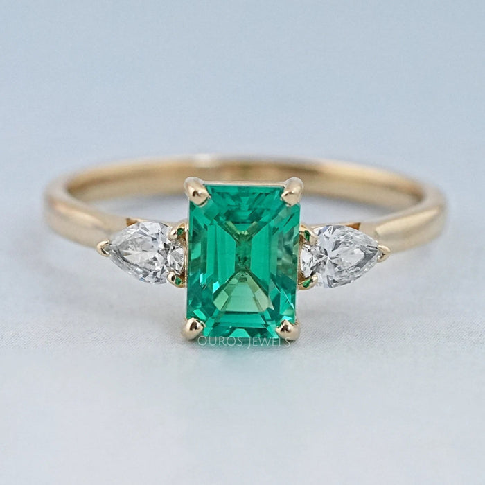 front view of green emerald gemstone and pear diamond three stone engagement ring