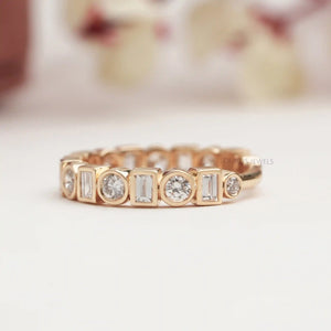 Side View of Baguette and Round Diamond Bezel Set Ring on white surface with blurred flora background.