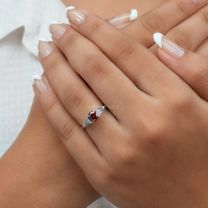 In finger front look of red round 3 stone engagement ring with 4 prong setting