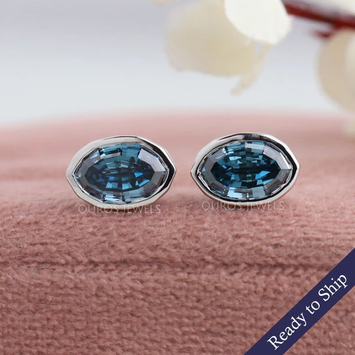 Front view of step cut blue oval diamond earrings set in bezel, crafted with 14k white gold.