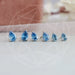 A close-up view Blue Pear Shaped Diamond Stud Earrings in five pairs. It arranged in a row on a light surface with a soft background.