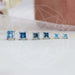 A Front View of Blue Diamond Princess Cut Earrings in line with Blurred Background.